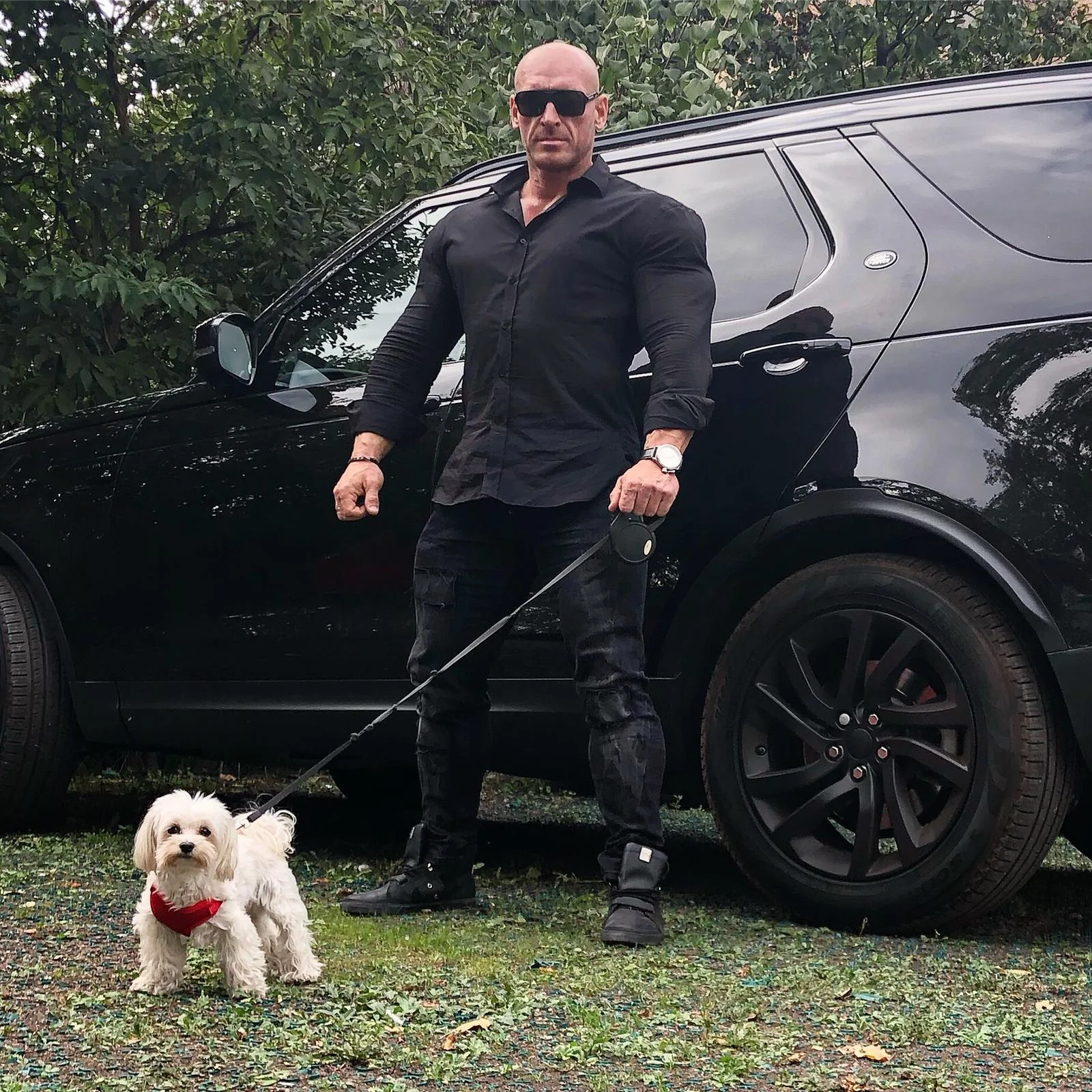 Muskulöser Mann in einem schwarzen Muscle-Fit-Hemd vor einem schwarzen SUV – der perfekte Casual-Look für Athleten
